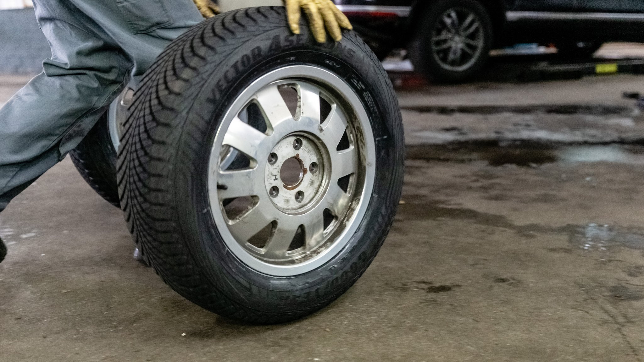 Ein Mitarbeiter rollt in einer Autowerkstatt in Bargteheide einen Ganzjahresreifen zu einem Auto.
