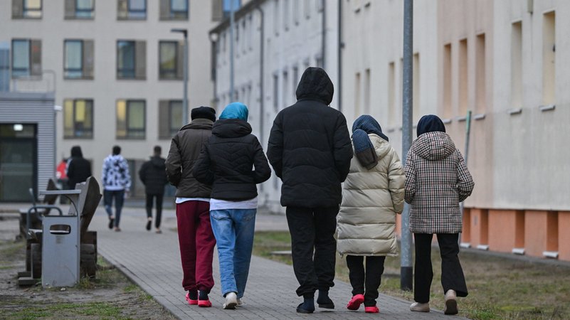 Migranten gehen über das Gelände einer Zentralen Erstaufnahmeeinrichtung für Asylbewerber. | Bild: dpa-Bildfunk/Patrick Pleul Migranten gehen über das Gelände einer Zentralen Erstaufnahmeeinrichtung für Asylbewerber.