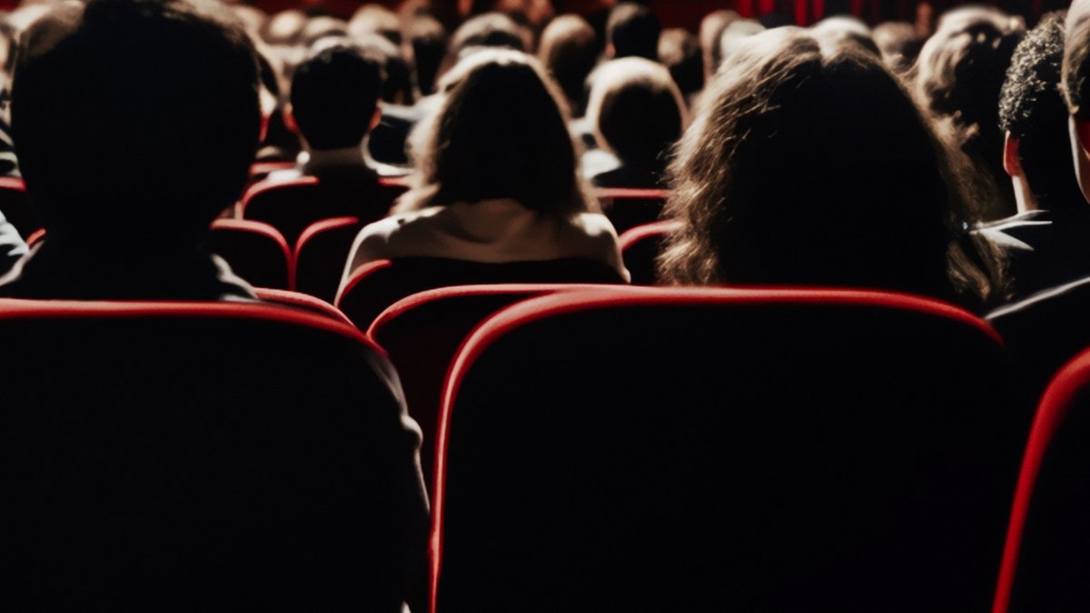 Menschen sitzen im Kinosaal vor einer weißen Leinwand.