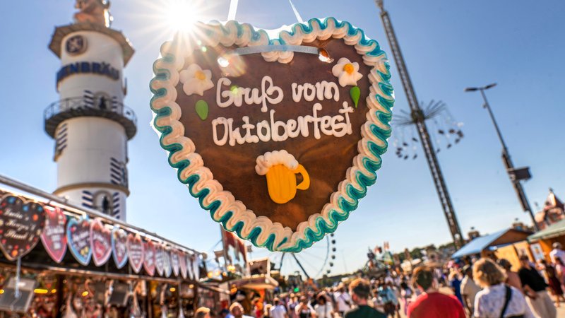 Nahaufnahme eines Lebkuchenherzes mit der Aufschrift "Gruß vom Oktoberfest" im Gegenlicht, dahinter Menschenmengen und Fahrgeschäfte | Bild: picture alliance / Wolfgang Maria Weber Nahaufnahme eines Lebkuchenherzes mit der Aufschrift "Gruß vom Oktoberfest" im Gegenlicht, dahinter Menschenmengen und Fahrgeschäfte