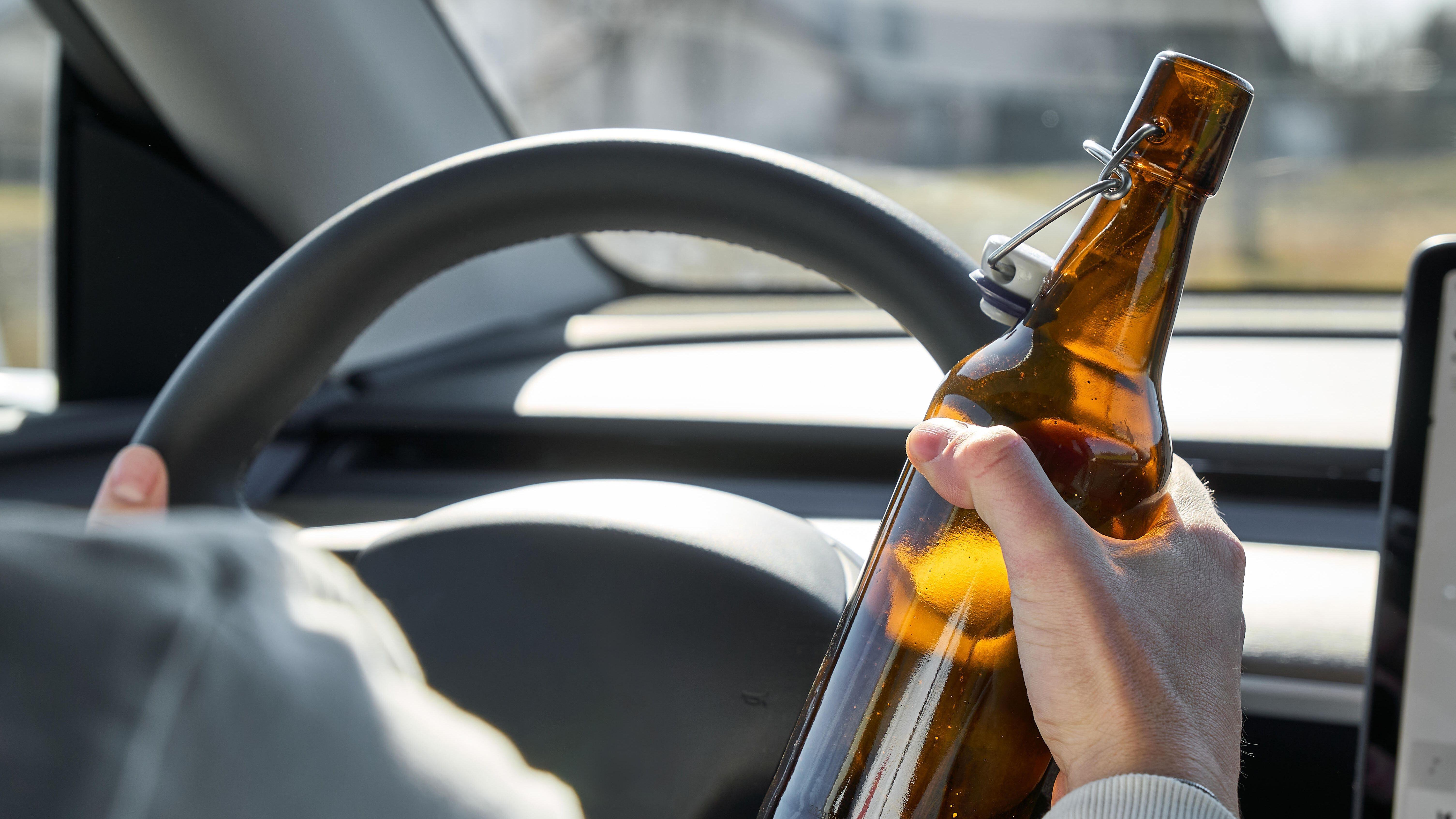 Ein Mann sitzt am Steuer und hält eine Bierflasche in der Hand. 