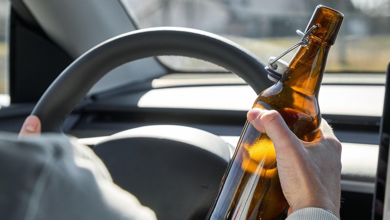 Ein Mann sitzt am Steuer und hält eine Bierflasche in der Hand. | Bild: picture alliance / CHROMORANGE | Michael Bihlmayer Ein Mann sitzt am Steuer und hält eine Bierflasche in der Hand.