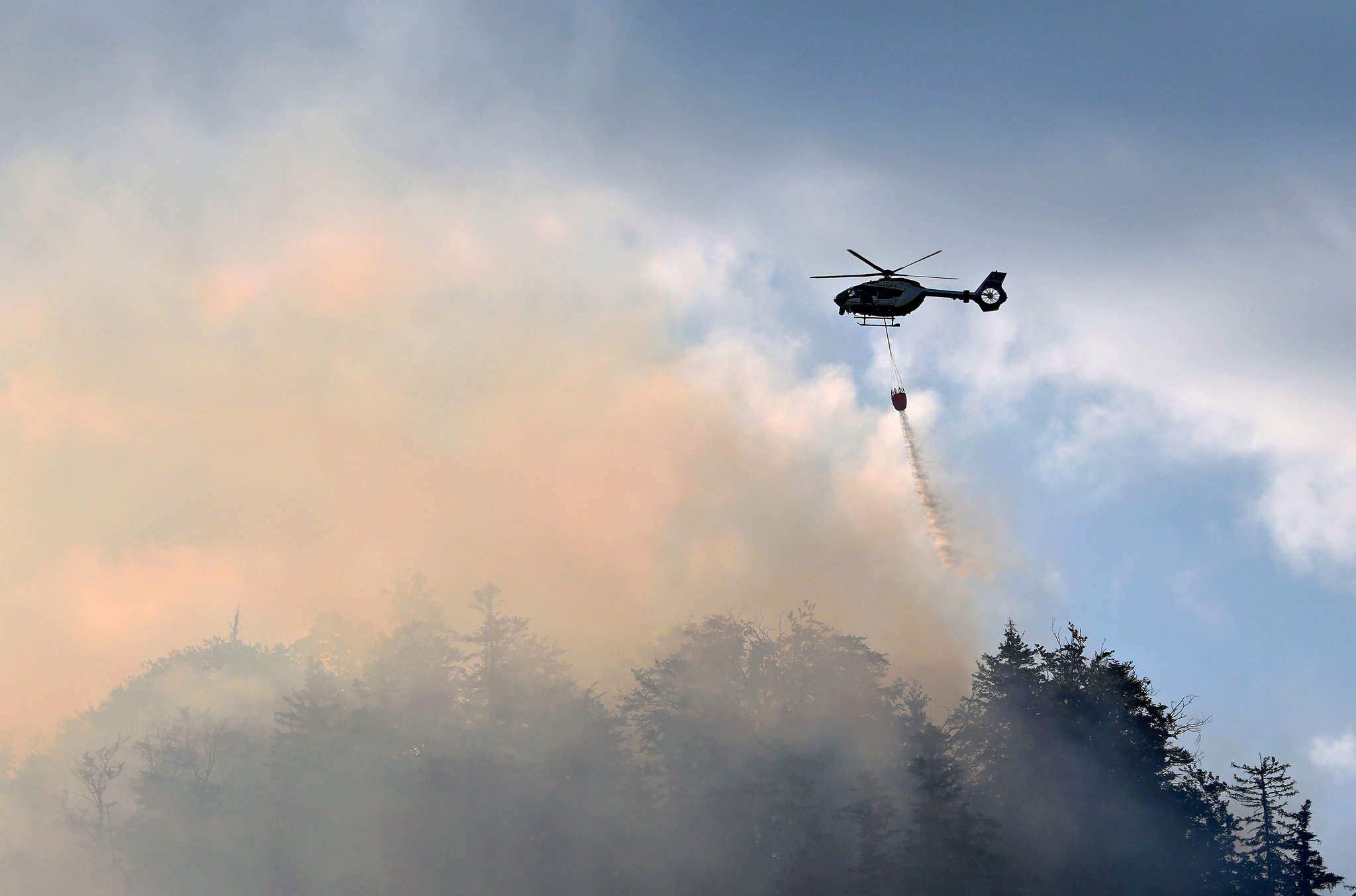 Ein Hubschrauber lässt zur Bekämpfung eines Brandes im Bergwald in den Chiemgauer Alpen Löschwasser ab.