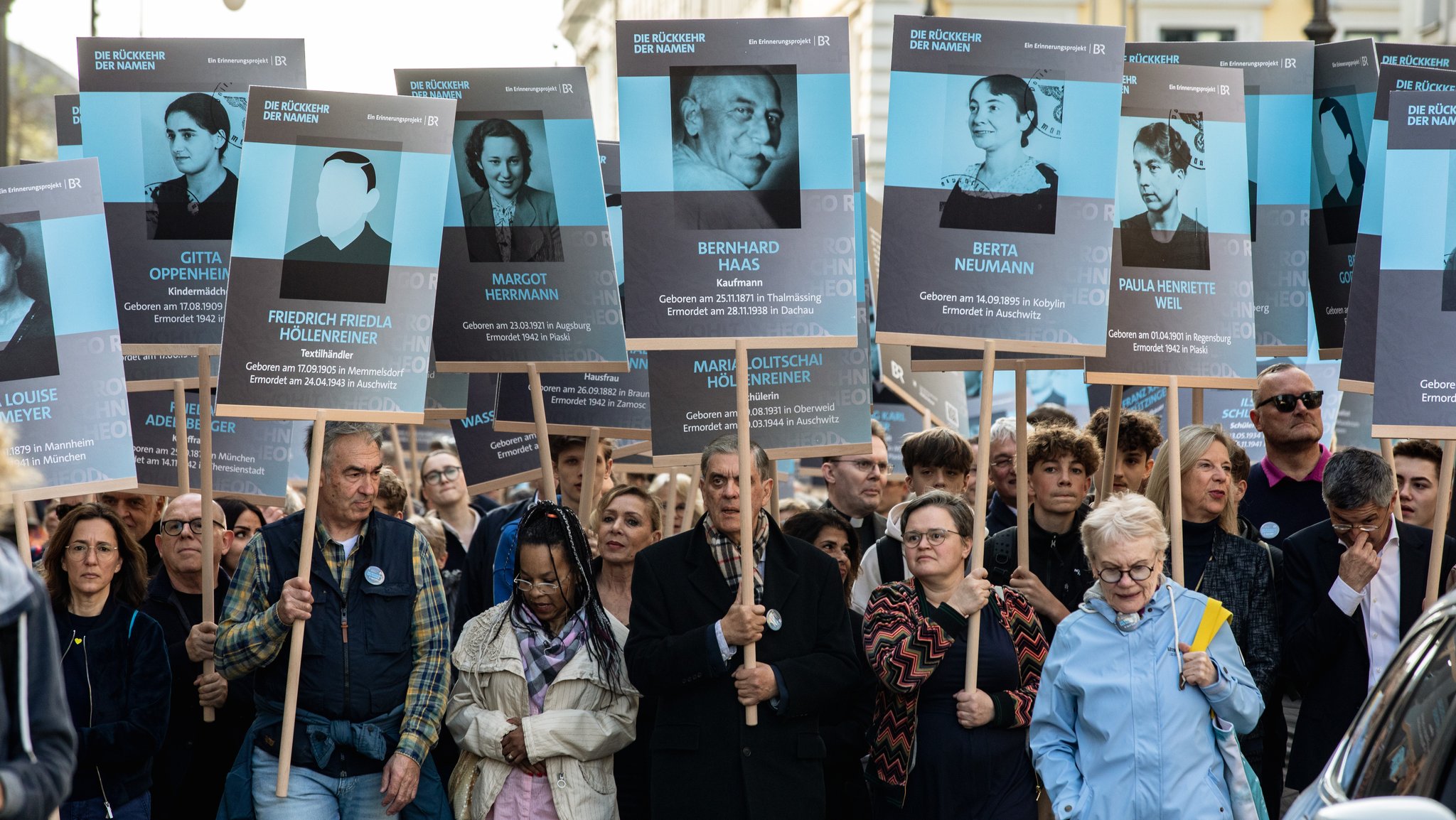 Menschen halten Schilder des Projekts "Die Rückkehr der Namen", darauf abgebildet Fotos und Namen von Ermordeten des Nazi-Regimes