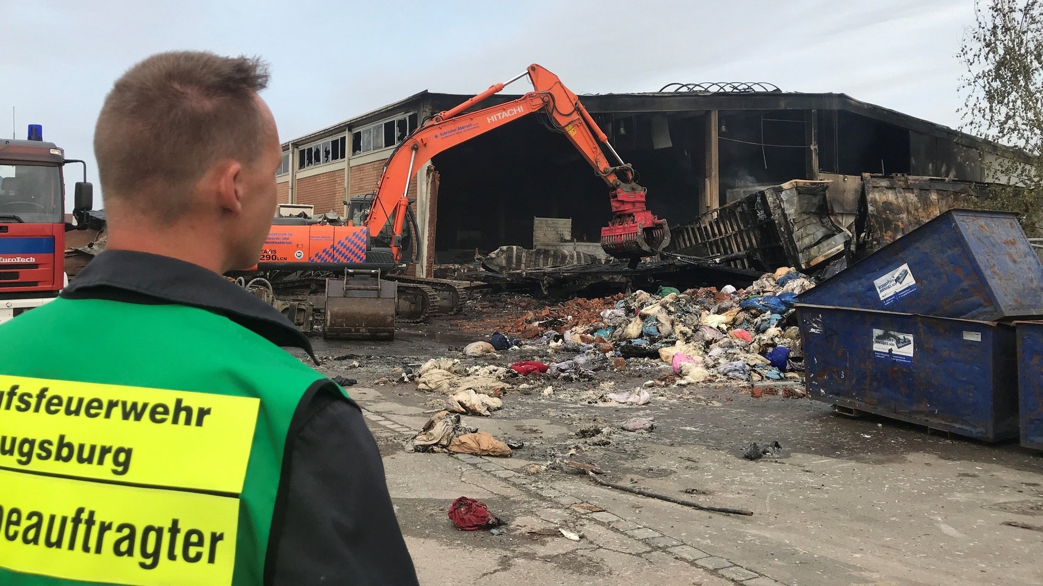 Ein Feuerwehrmann steht vor der zerstörten Halle, die gestern Feuer gefangen hat.