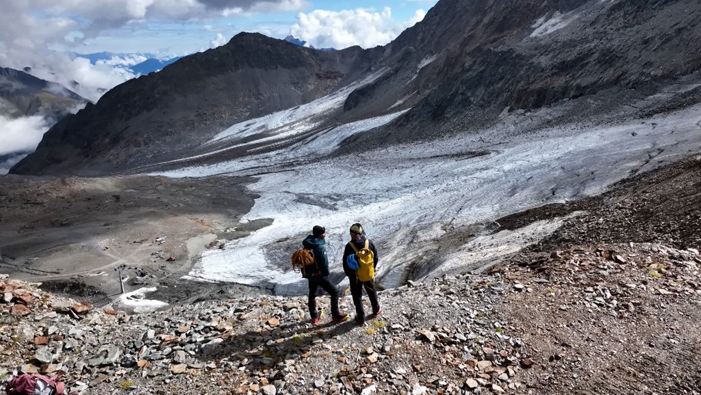 Zwei Menschen in Outdoor-Kleidung stehen vor einem Gletscher im Hochgebirge