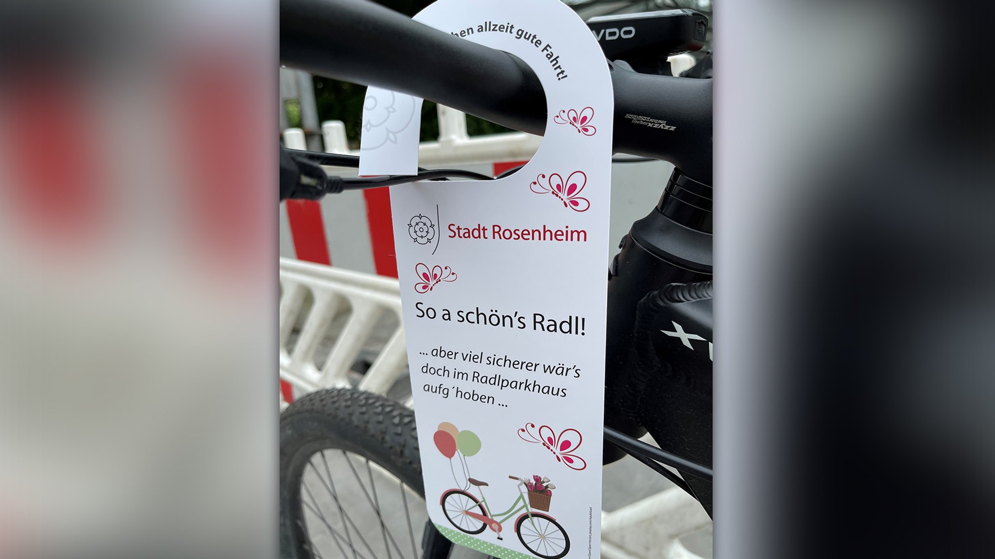 Auf einem Anhänger an einem abgestellten Fahrrad steht: "So a schön's Radl! ... aber viel sicherer wär's doch im Radlparkhaus aufg'hoben ..."