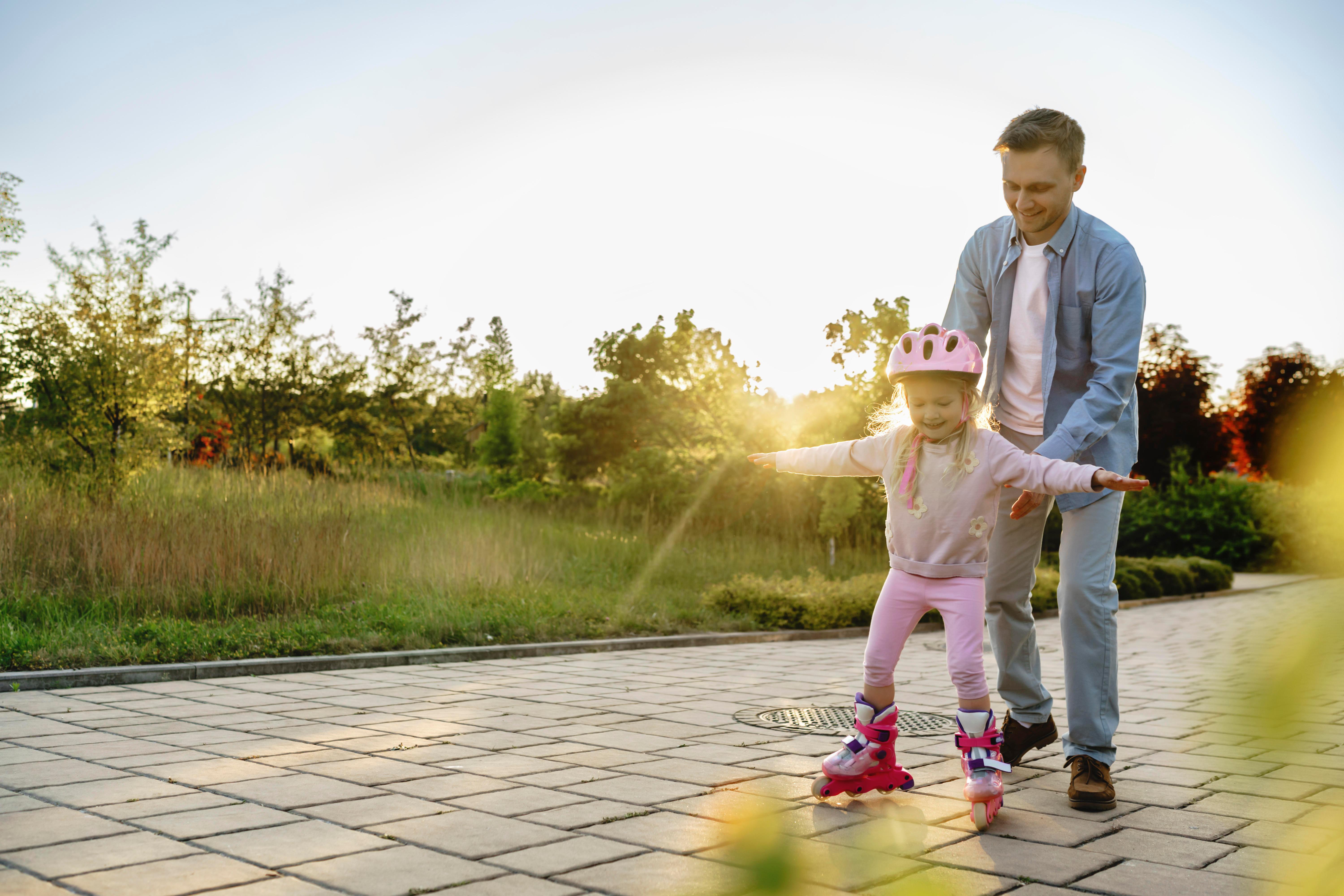 Ein Vater mit seiner Tochter, die Inline-Skates fährt (Symbolbild)