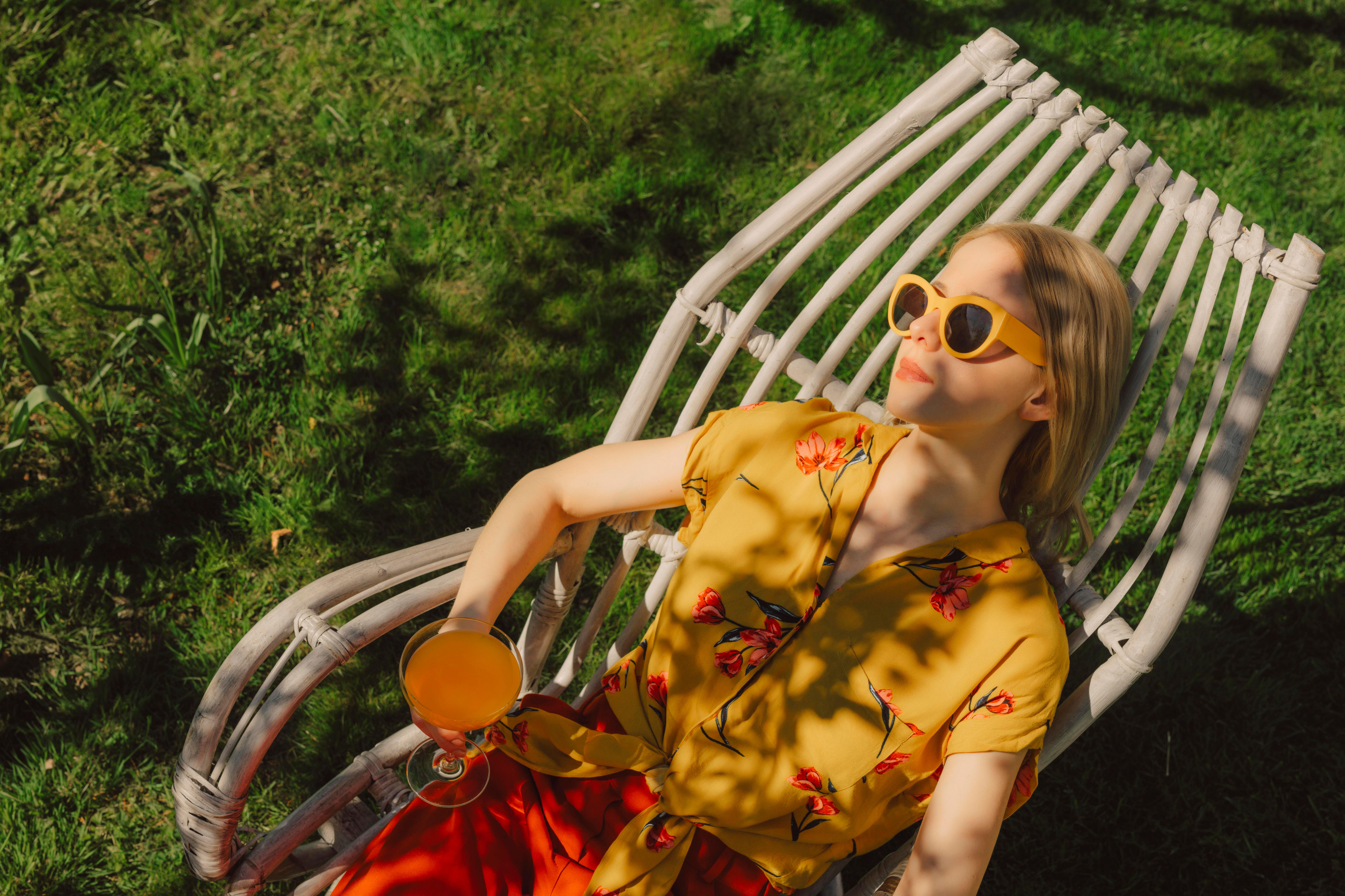 Frau liegt in einem Gartenstuhl mit Cocktail in der Hand