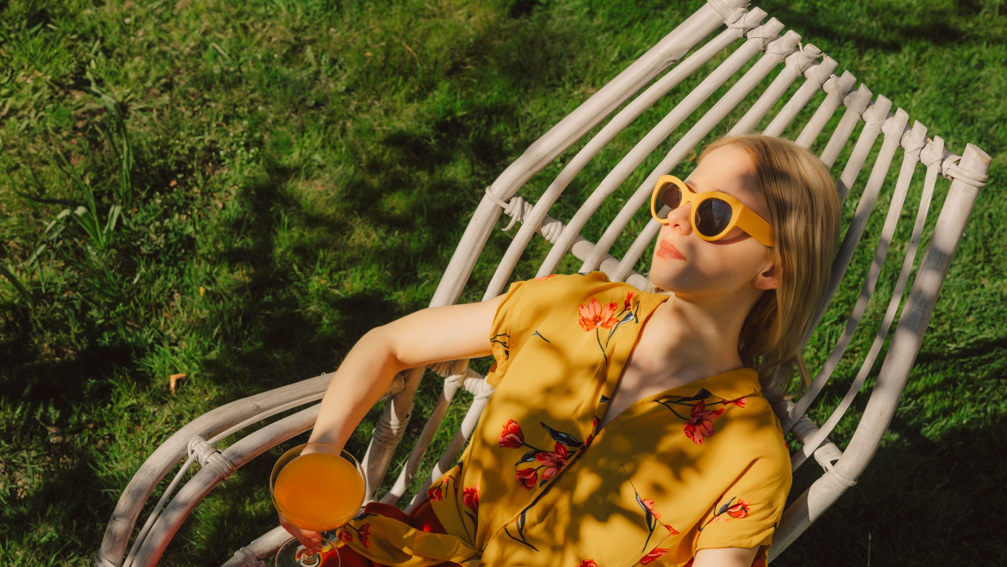 Frau liegt in einem Gartenstuhl mit Cocktail in der Hand