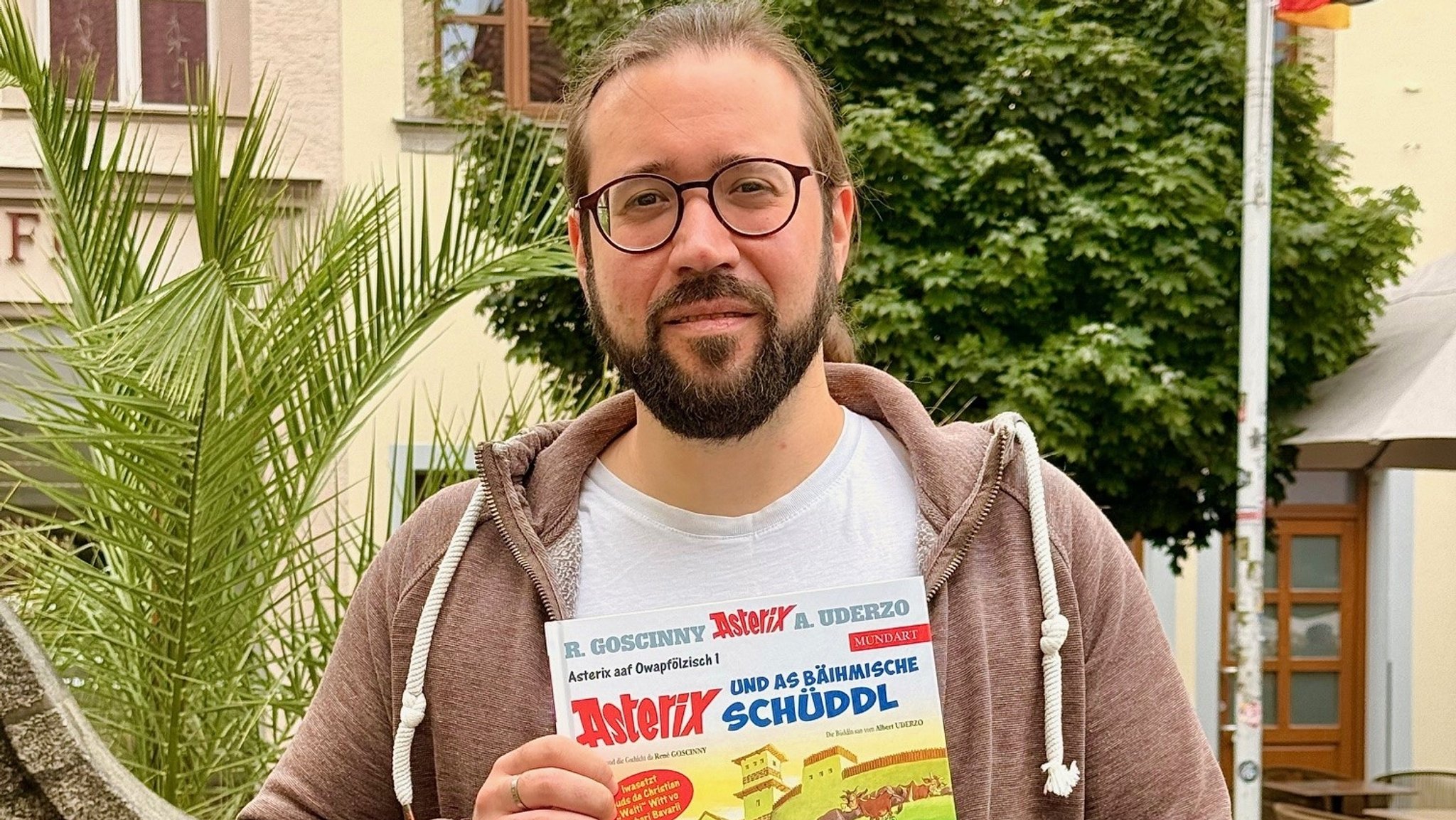 Autor Christian Witt hält eine Ausgabe "Asterix und as bäihmische Schüddl" in der Hand. | Bild: BR/Rudolf Heinz Autor Christian Witt hält eine Ausgabe "Asterix und as bäihmische Schüddl" in der Hand.