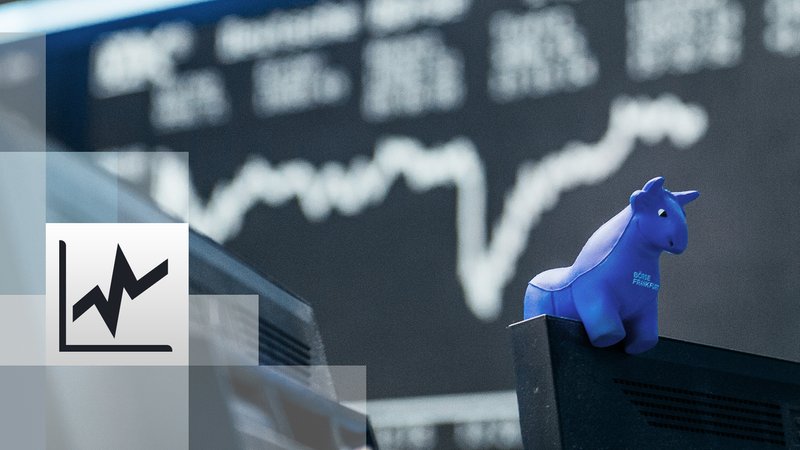Ein blauer Stier aus Gummi sitzt auf der oberen Kante eines Bildschirmes, im Hintergrund die Kurstafel der Börse