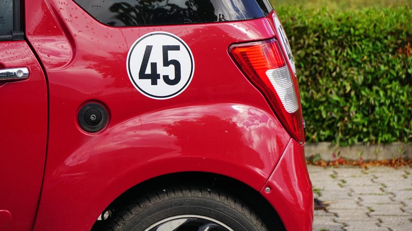 Ein rotes Mopedauto auf dem großer Aufkleber mit der Zahl 45 klebt. | Bild: picture alliance / CHROMORANGE | Elke Münzel Ein rotes Mopedauto auf dem großer Aufkleber mit der Zahl 45 klebt.
