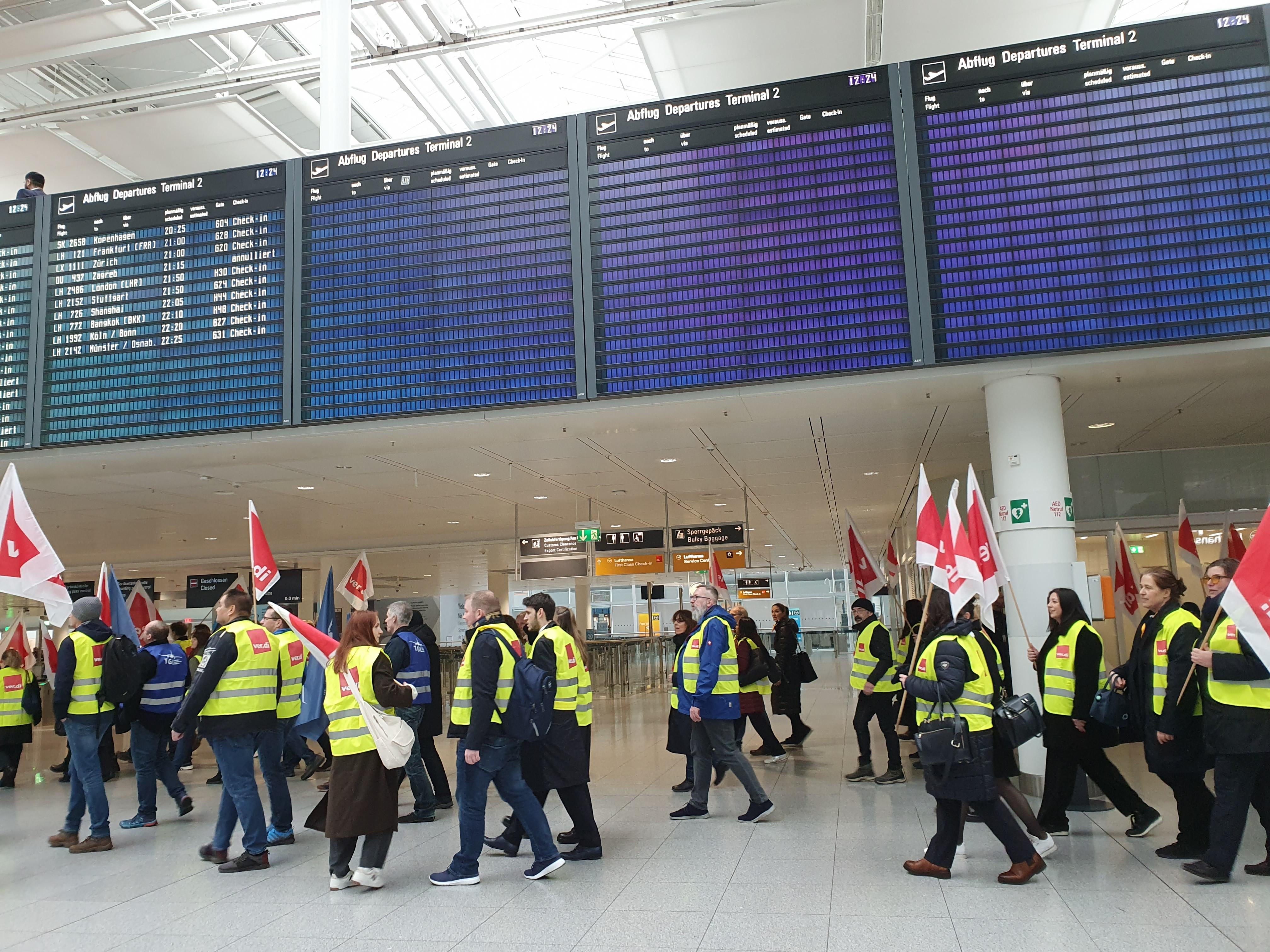 Warnstreikende ziehen durchs Terminal 2 vorbei an leeren Anzeigetafeln.