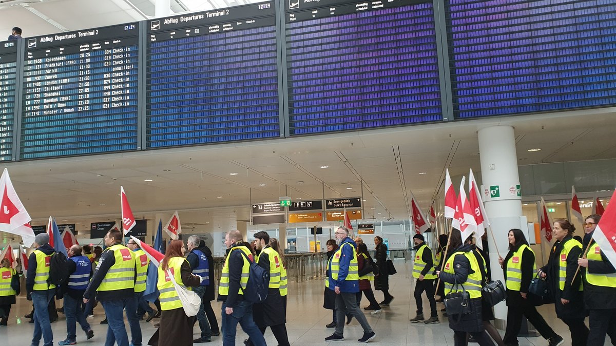 Warnstreikende ziehen durchs Terminal 2 vorbei an leeren Anzeigetafeln.