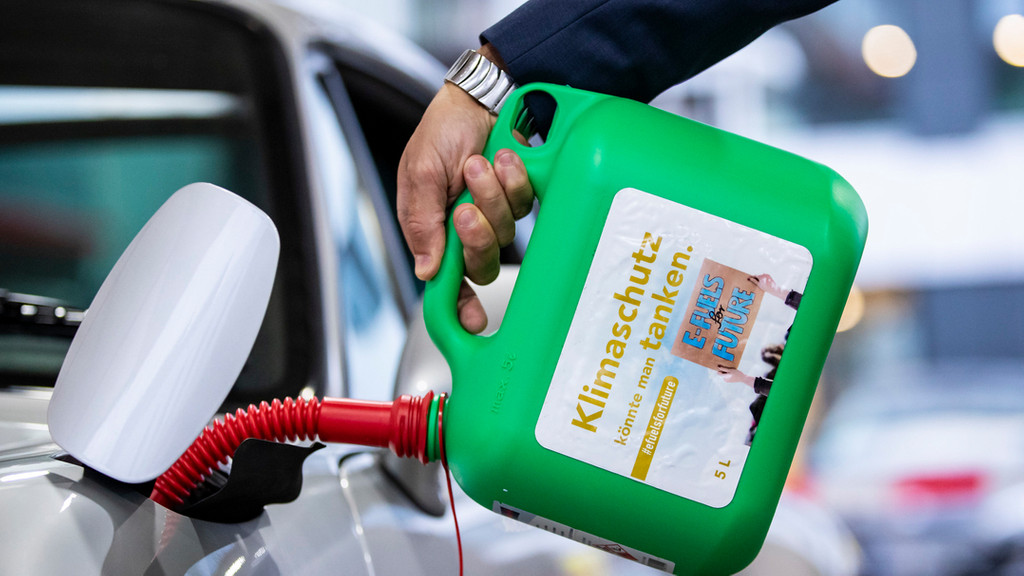 in Auto wird mit einem Kanister mit der Aufschrift "Klimaschutz könnte man Tanken - E-Fules for Future" an einer Tankstelle mit E-Fuel betankt.