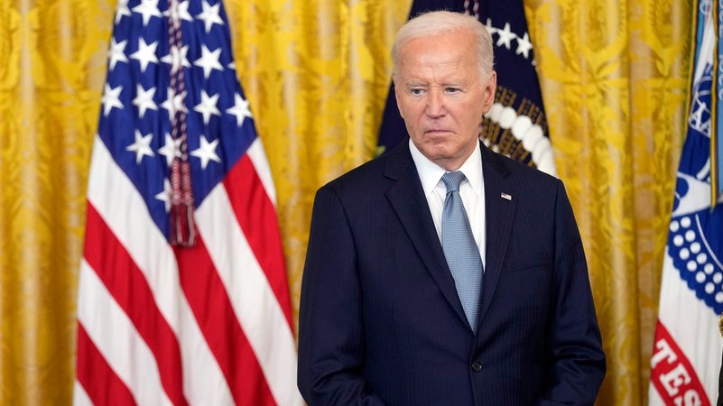 US-Präsident Joe Biden hört bei einer Zeremonie zu, die Hände gefaltet, den Blick nach unten gerichtet