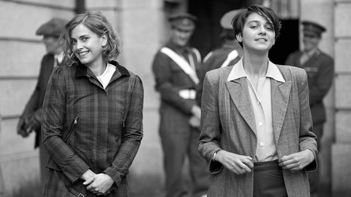 Zwei junge Frauen in historischer Kleidung lächeln auf einem Schwarz-Weiß-Foto in die Kamera. 