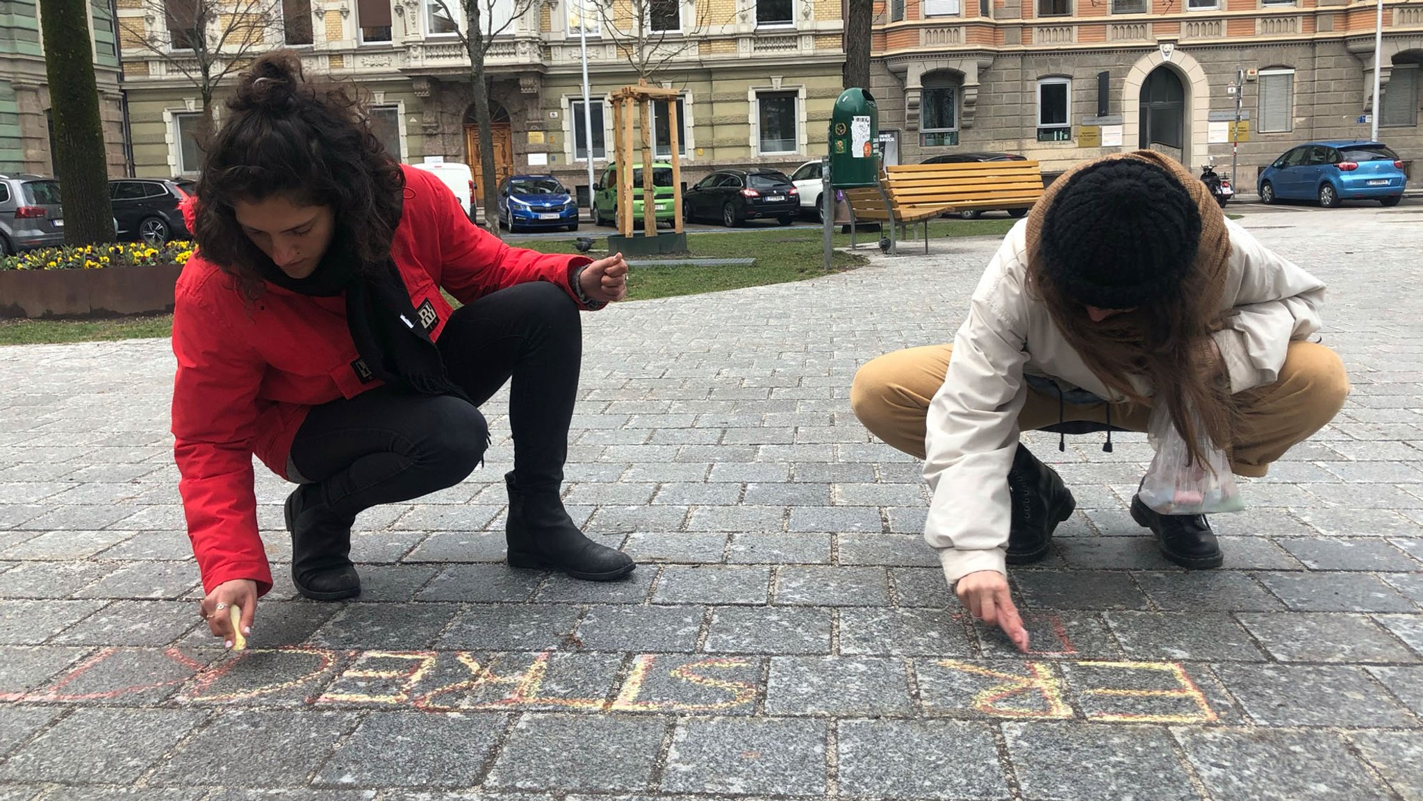 Paula Jorge und Kim Hesterberg gehen zum Adolf-Pichler-Platz, wo die sexualisierte Belästigung stattgefunden hat. Mit bunten Kreiden schreiben sie diese dort auf den Asphalt. 