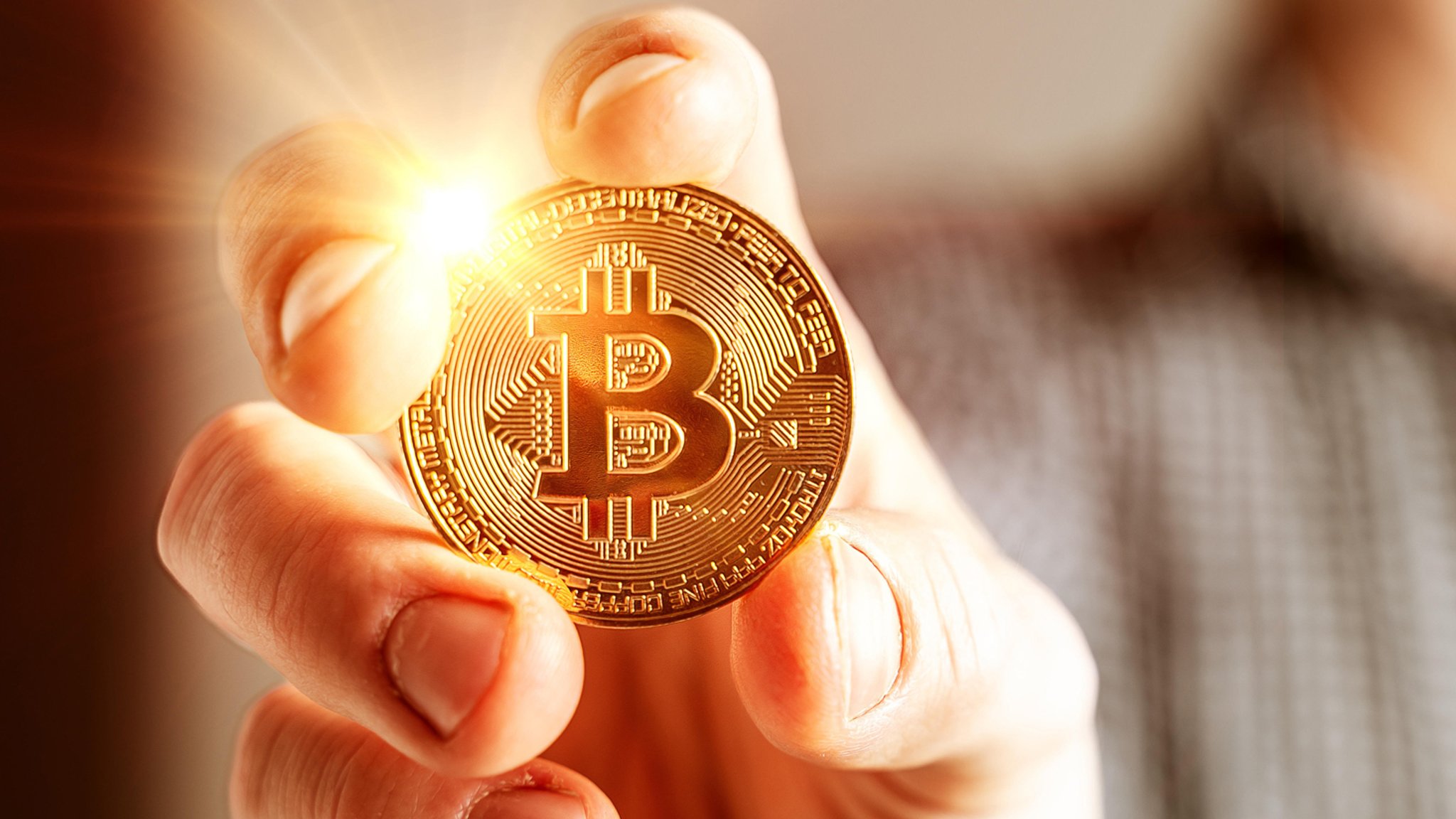 Goldene leuchtende Bitcoin Münze in der Hand eines Mannes
