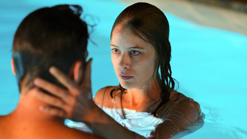 Ein Paar steht in einem blau beleuchteten Schwimmbecken zusammen und blickt sich an (Filmszene aus "Undine")