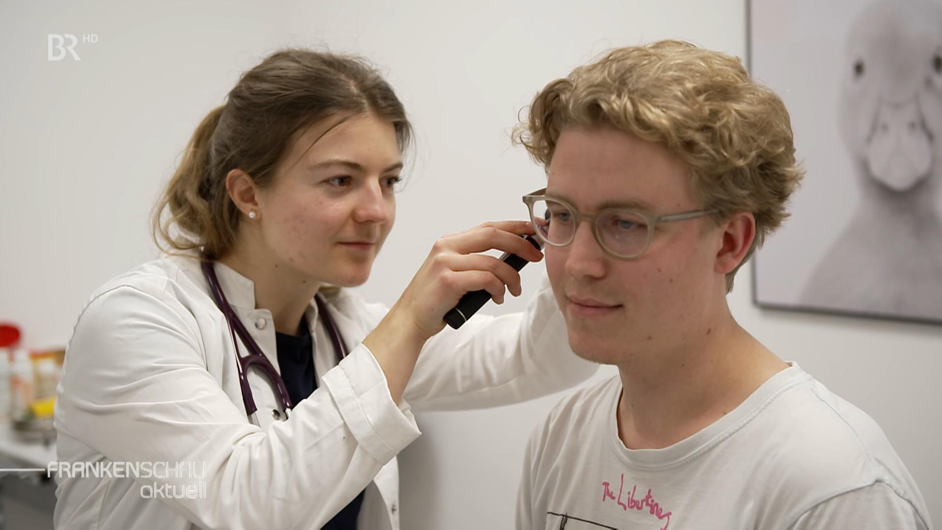 Eine junge Ärztin schaut in das Ohr eines Patienten. 