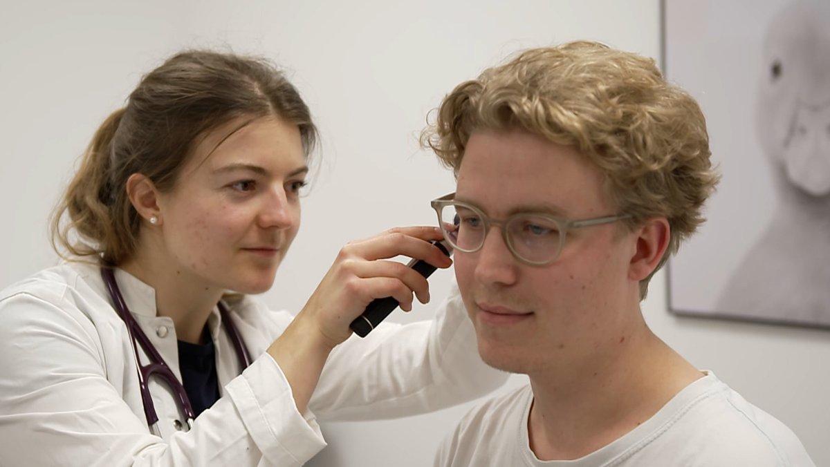 Eine junge Ärztin schaut in das Ohr eines Patienten. 