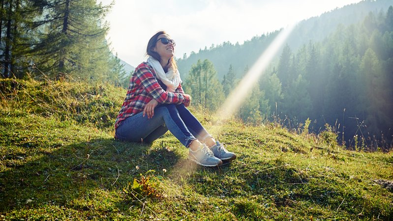 Frau sitzt im Herbst auf einem Hügel und lässt sich die Sonne ins Gesicht scheinen.