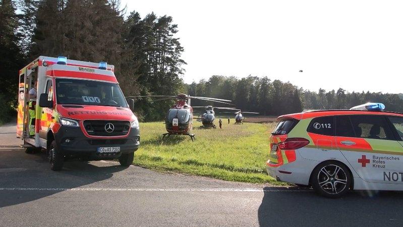 Auf einer Landstraße stehen zwei Rettungswagen, auf der Wiese daneben drei Hubschrauber, dazwischen bewegen sich Rettungskräfte.