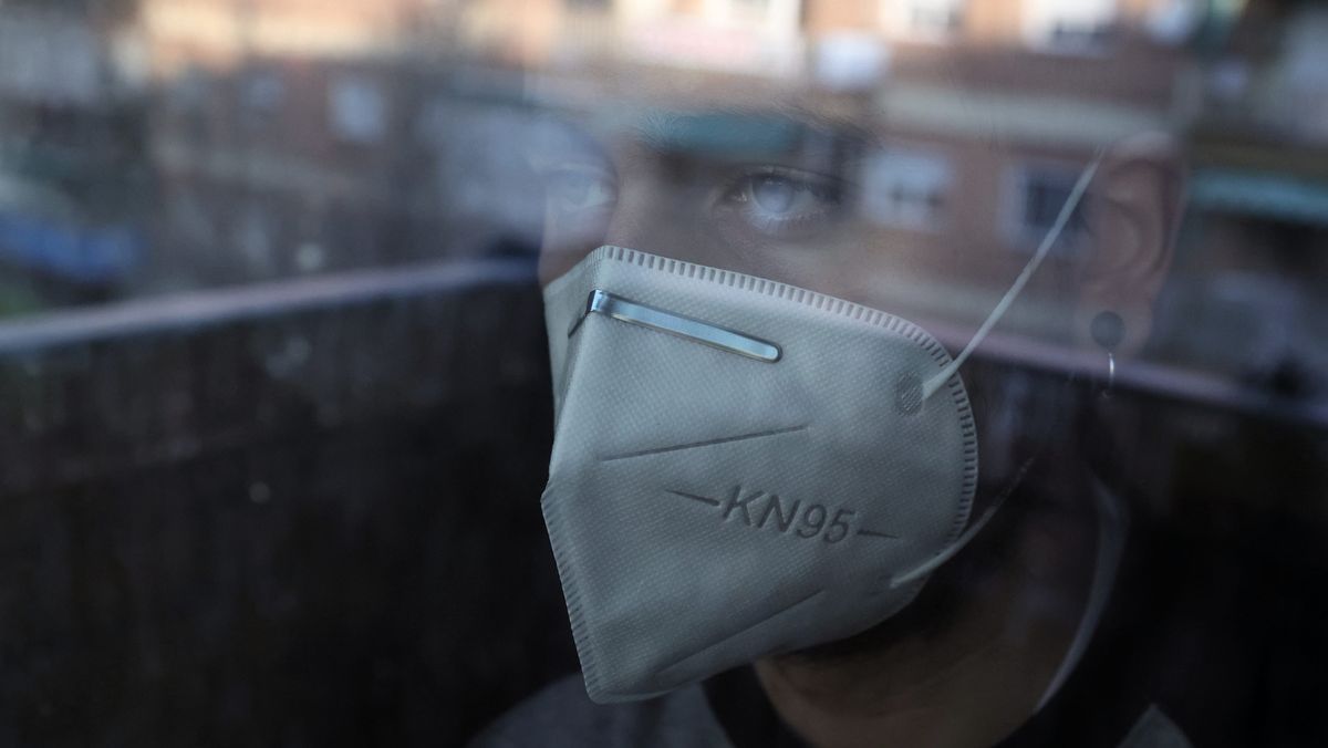 Ein Mann mit Maske blickt durch eine Scheibe nach draußen (Symbolbild)