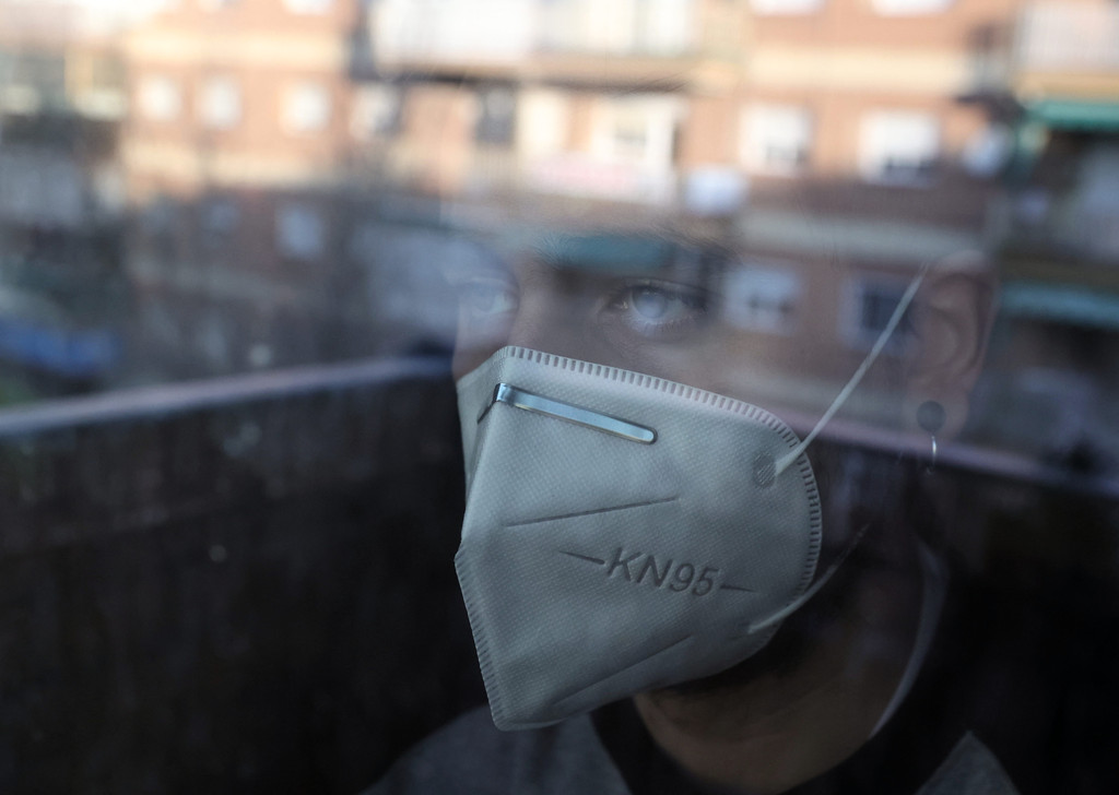 Ein Mann mit Maske blickt durch eine Scheibe nach draußen (Symbolbild)