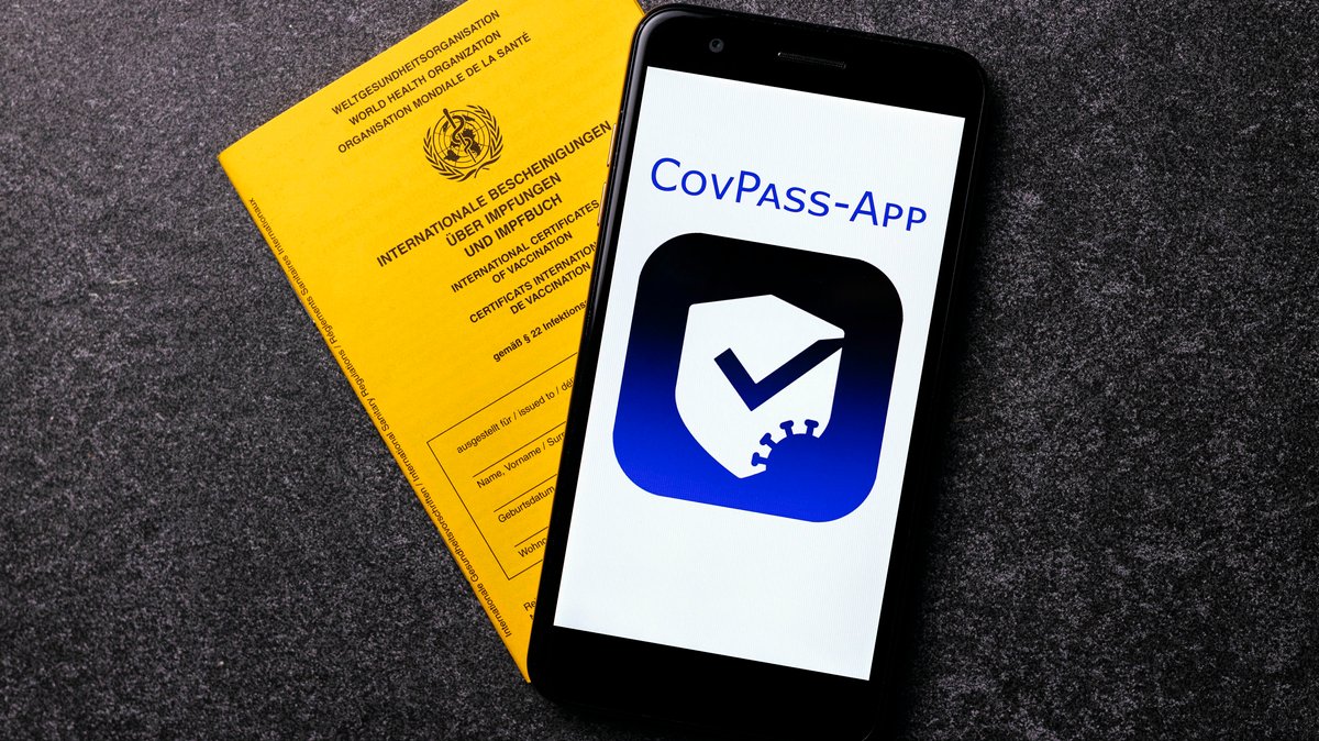 Die in Deutschland geplante "CovPass-App" auf einem Smartphone-Bildschirm neben einem traditionellen Impfausweis, aufgenommen am 28.05.21.