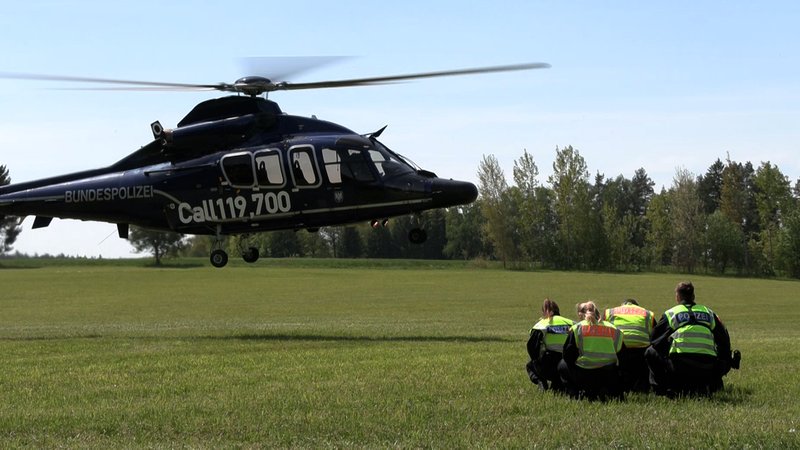 Vier Polizistinnen und Polizisten kauern in Warnwesten auf einer Wiese, während neben ihnen ein Hubschrauber landet. Die Bundespolizei setzt auch Hubschrauber zur Überwachung der Grenzen ein. | Bild: BR/Margit Ringer Vier Polizistinnen und Polizisten kauern in Warnwesten auf einer Wiese, während neben ihnen ein Hubschrauber landet. Die Bundespolizei setzt auch Hubschrauber zur Überwachung der Grenzen ein.