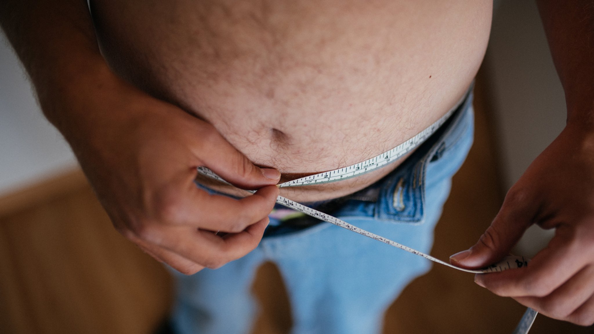 Ein Mann misst mit einem Maßband seinen Bauch.