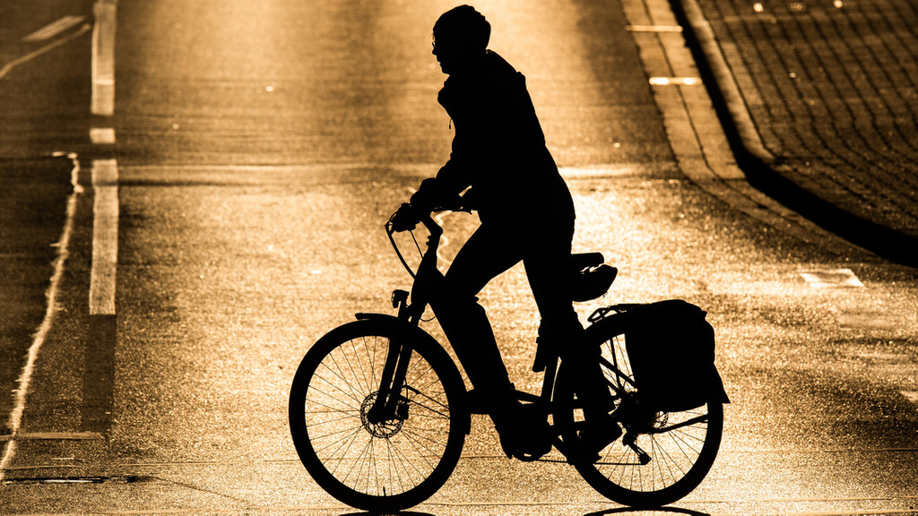 Eine Frau fährt bei Sonnenaufgang mit einem Fahrrad über eine Straße
