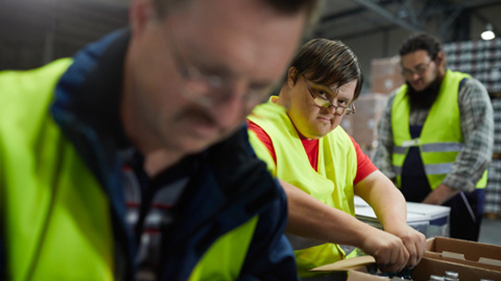 Drei Männer mit gelber Warnweste arbeiten in einer Werkstatt der Lebenshilfe.