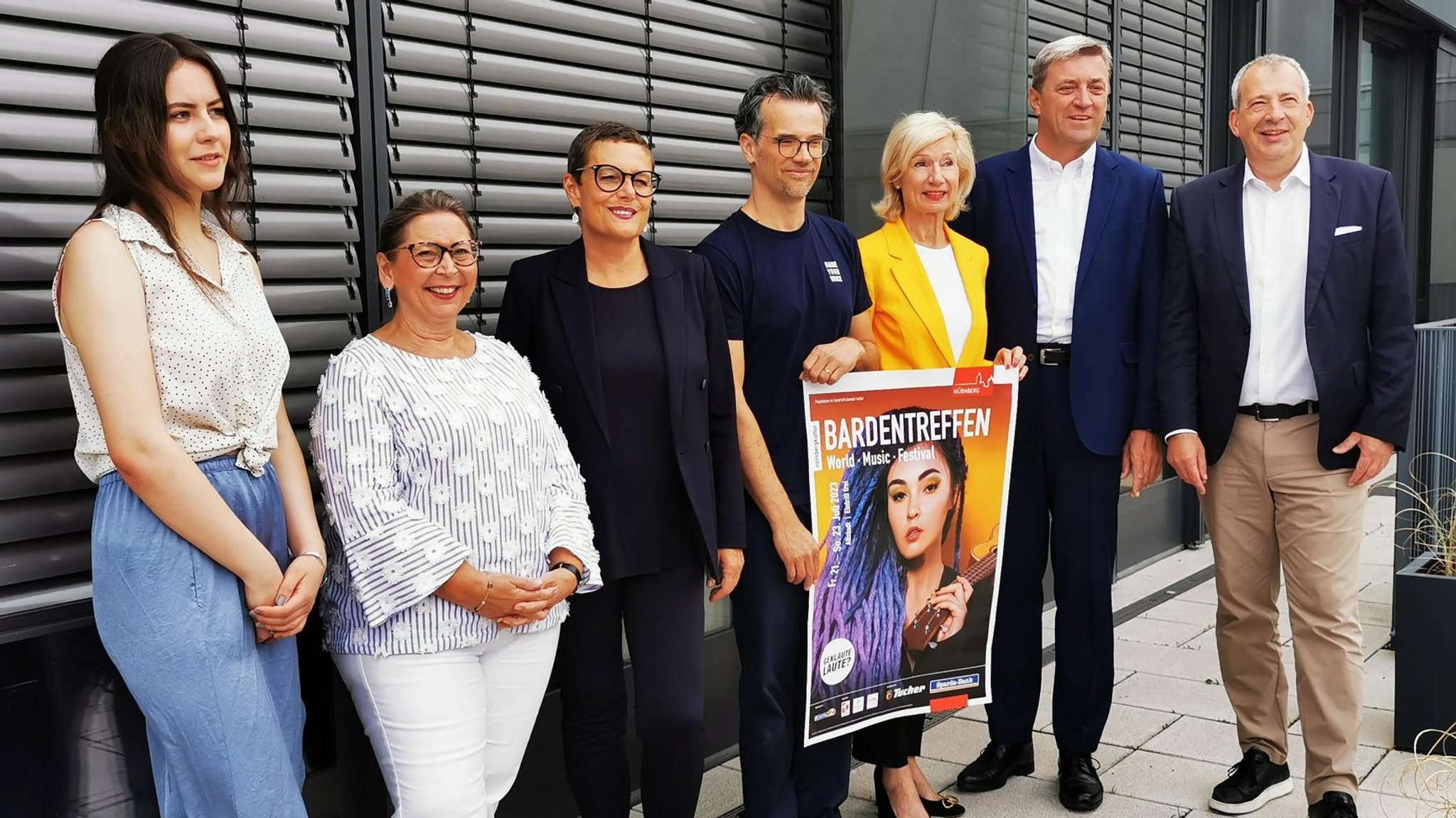 Männer und Frauen präsentieren ein Plakat des Bardentreffens 2023.