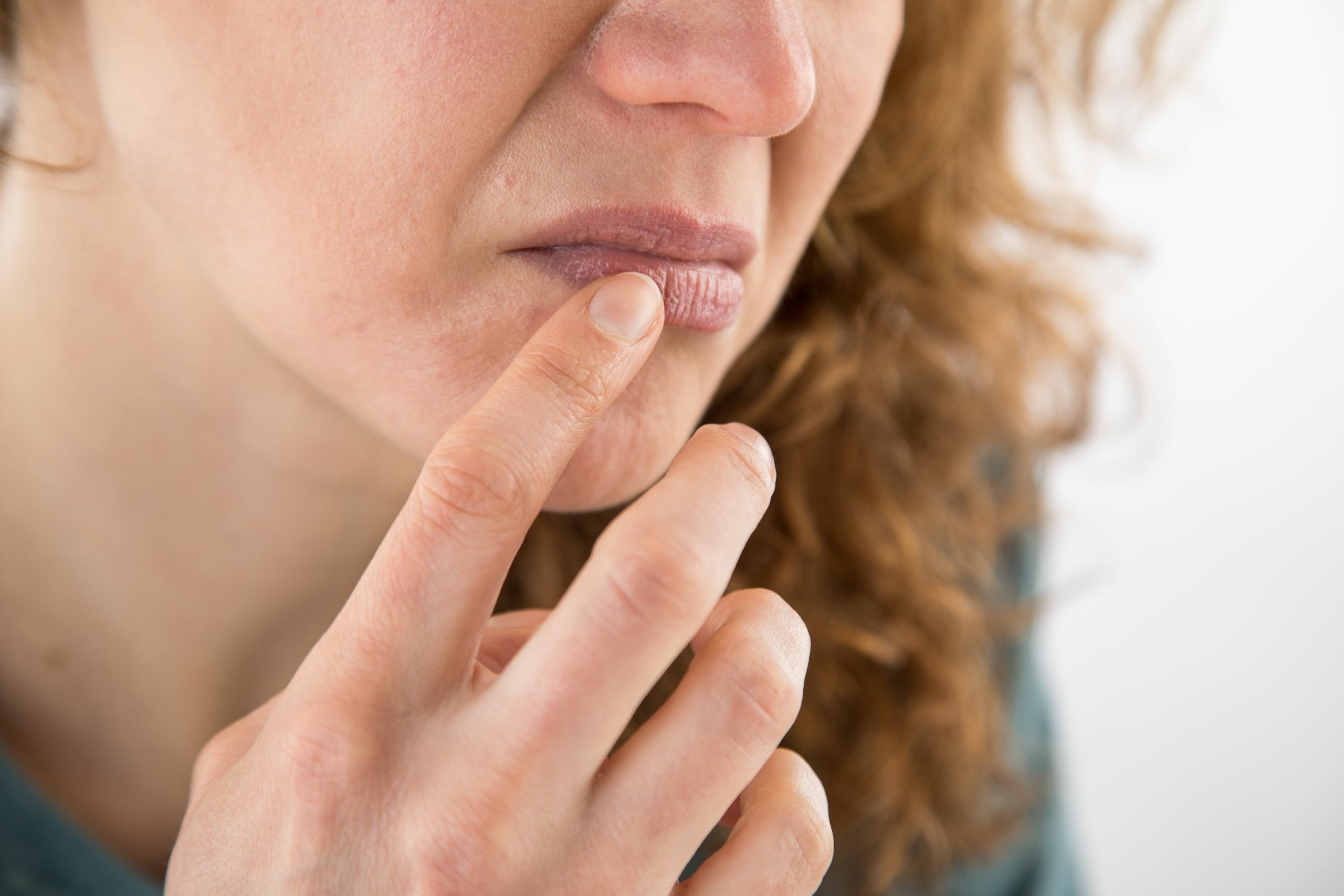 Frau fasst sich mit dem Finger an die Lippen