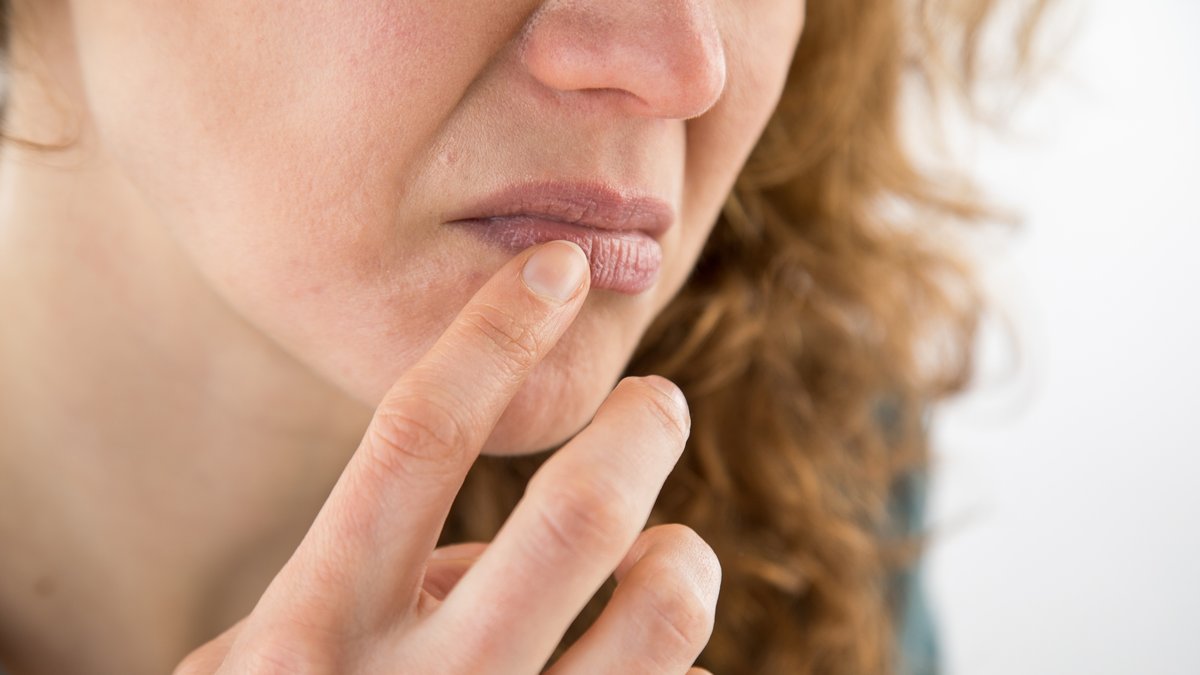 Frau fasst sich mit dem Finger an die Lippen