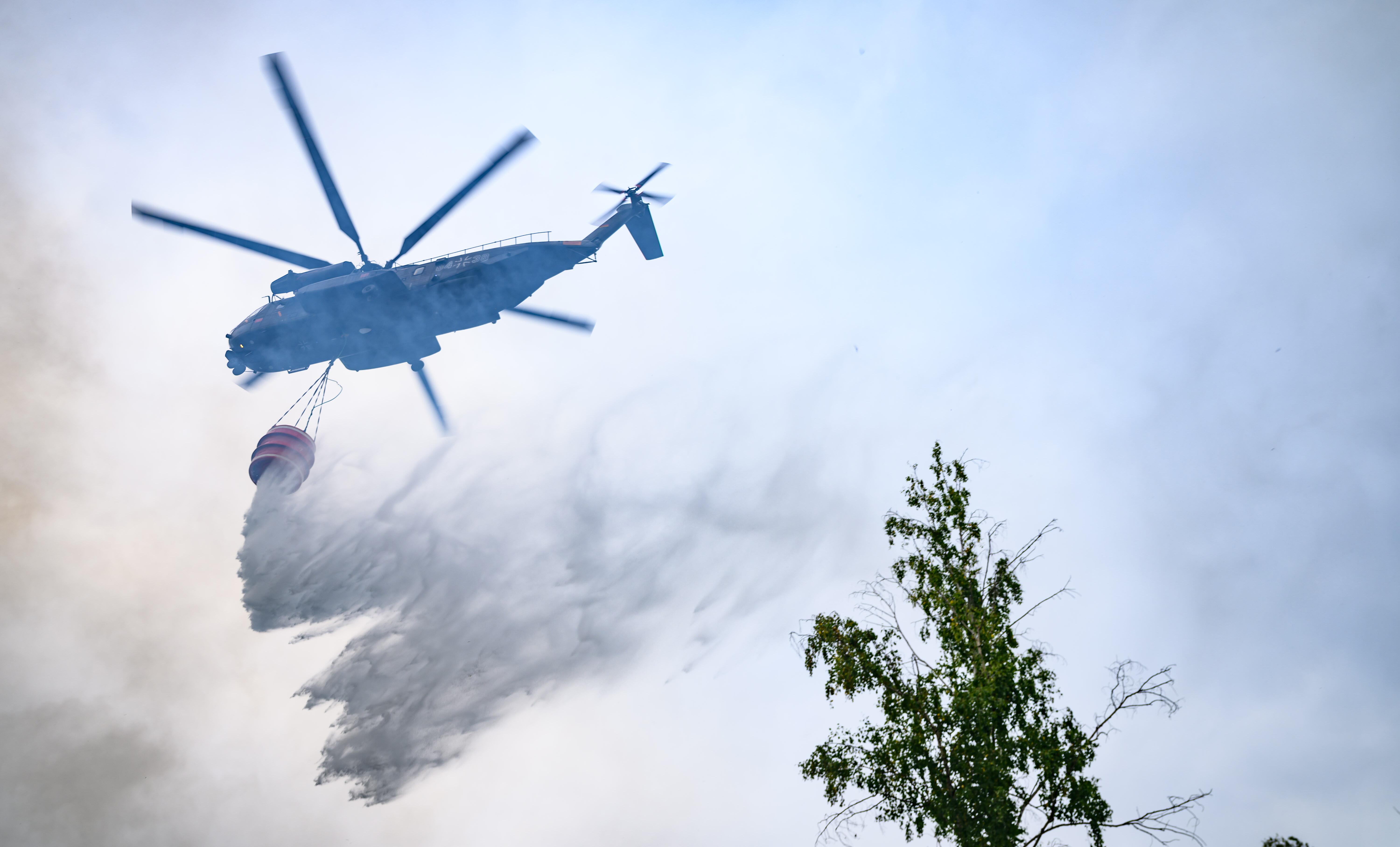 (Symbolbild) Ein Löschhubschrauber der Bundeswehr lässt Wasser über einem Waldstück ab.