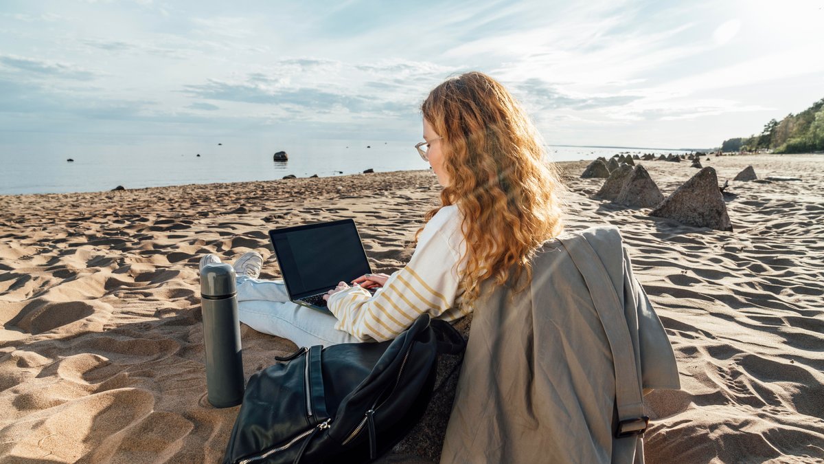 Eine junge Frau sitzt mit einem Laptop am Strand