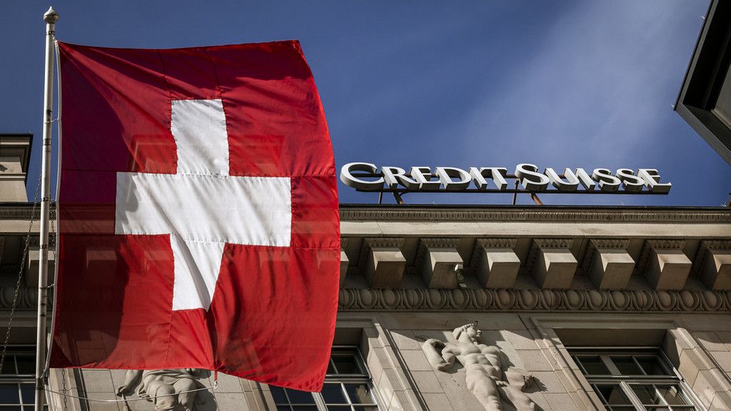 18.03.2023, Schweiz, Luzern: Die Flagge der Schweiz weht neben dem Logo der Schweizer Bank Credit Suisse. Die Lage der angeschlagenen Schweizer Großbank hat am Samstag (18.03.) die Regierung auf den Plan gerufen.