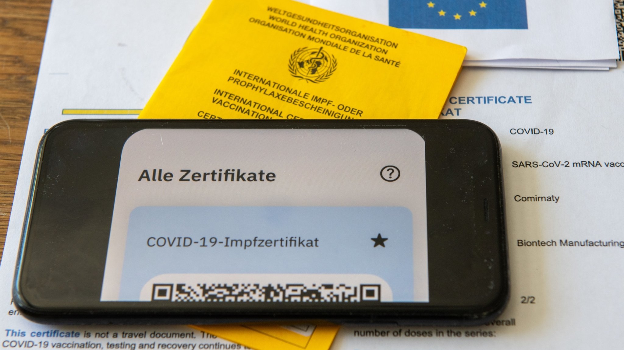 Ein Impfpass und ein Smartphone, auf dem die App CovPass läuft, liegen auf einem Impfzertifikat.