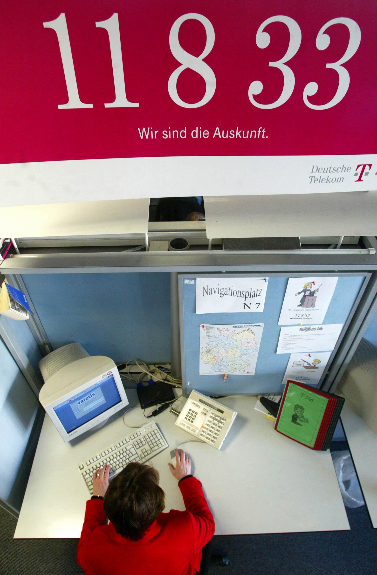 Ein Plakat der Telekom-Auskunft 11833 hängt über einem Büroarbeitsplatz.