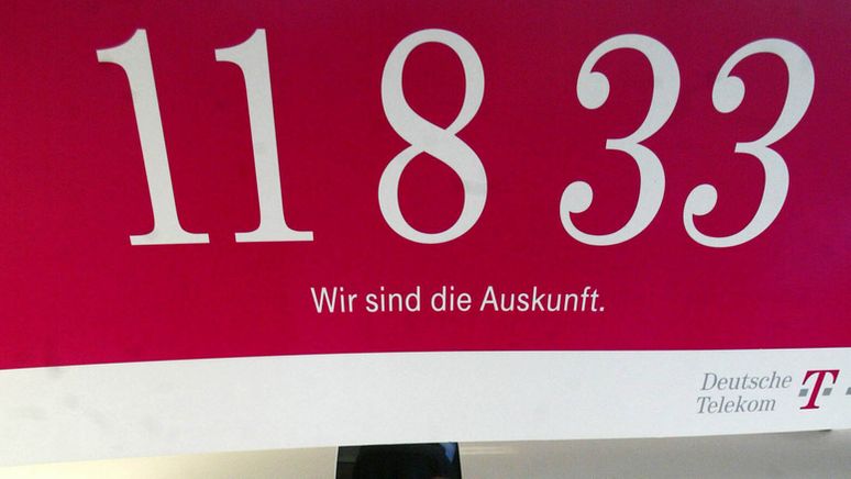 Ein Plakat der Telekom-Auskunft 11833 hängt über einem Büroarbeitsplatz. | Bild:picture-alliance/ ZB | Jens Wolf