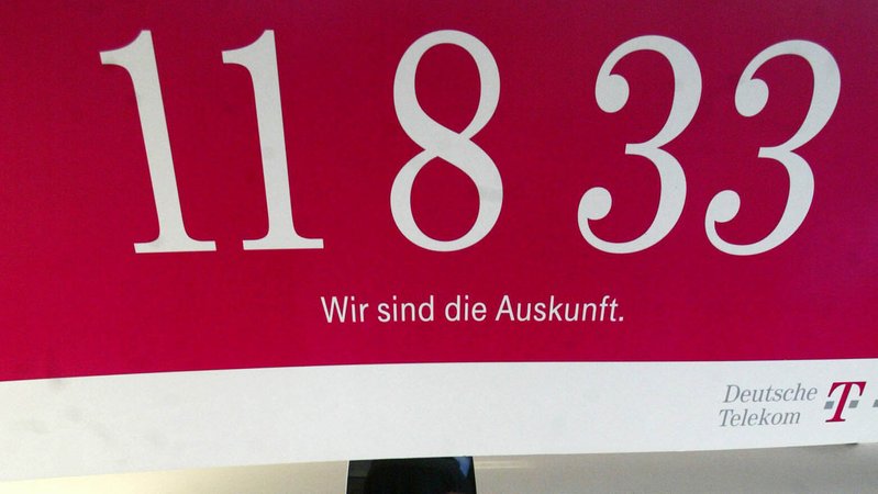 Ein Plakat der Telekom-Auskunft 11833 hängt über einem Büroarbeitsplatz.
