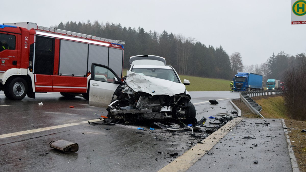 Bayern, Tännesberg: Ein Einsatzfahrzeug der Feuerwehr steht neben einem stark demolierten Unfallfahrzeug.