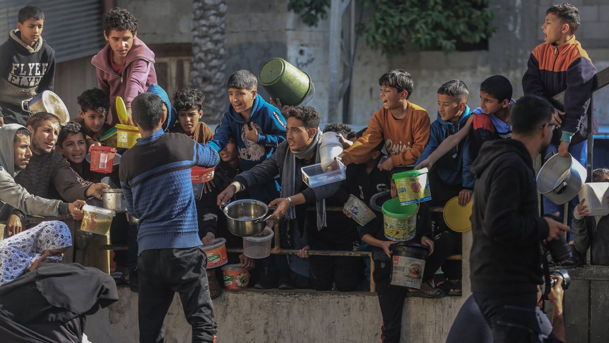 Palästinenser versammeln sich mit Töpfen, um an einer von einer Wohltätigkeitsorganisation eingerichteten Spendenstelle Lebensmittel entgegenzunehmen.