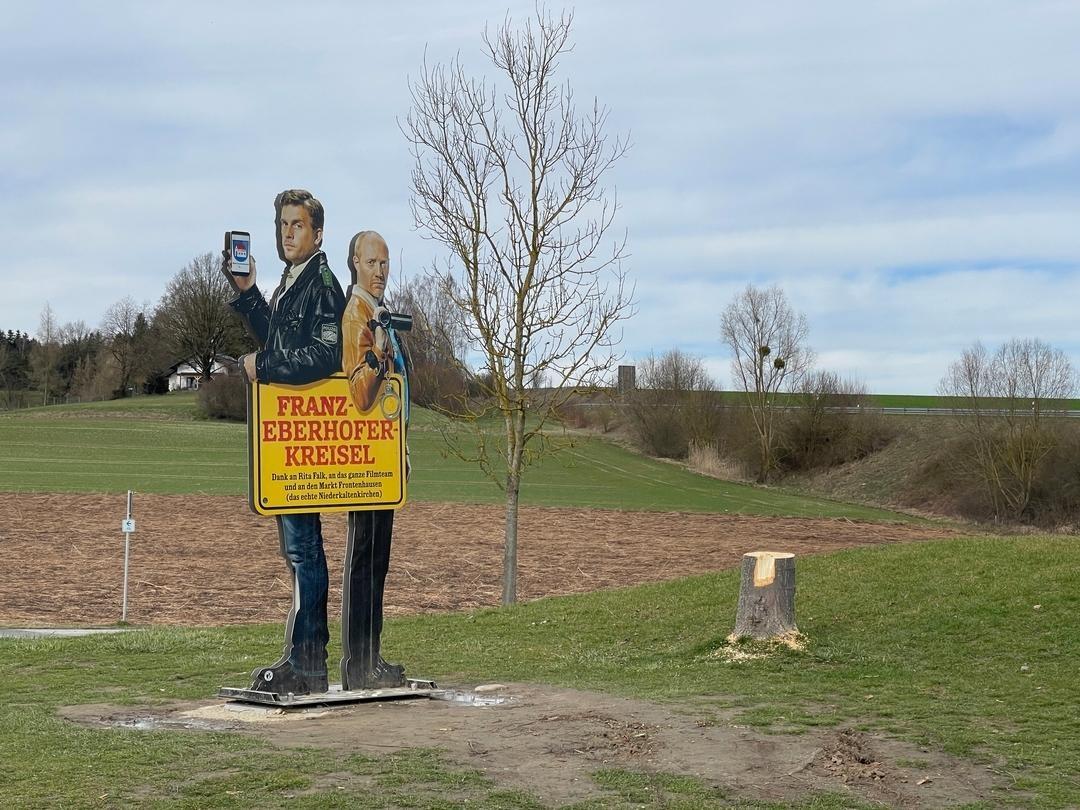 Baumstumpf neben Hinweisschild auf "Franz-Eberhofer-Kreisel"