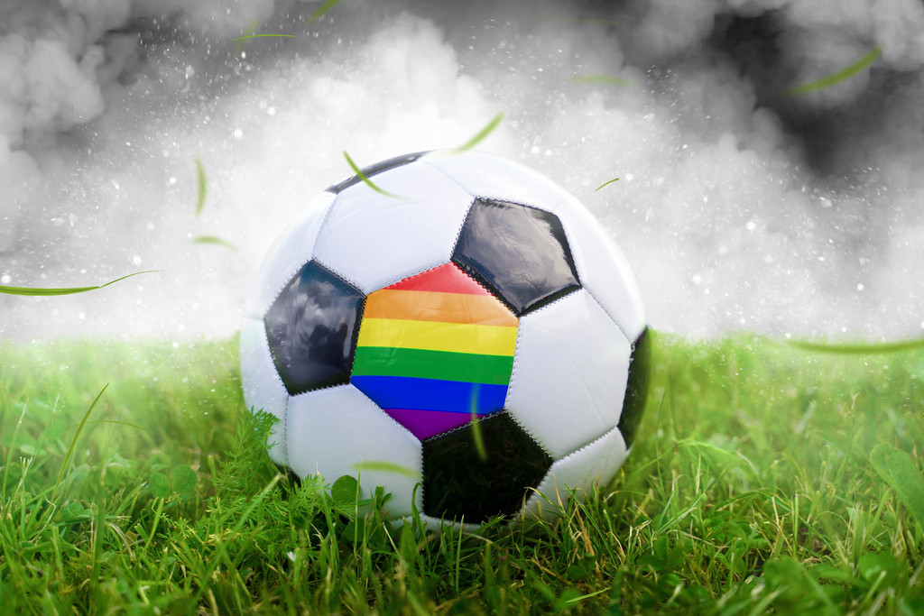 Fußball auf Spielfeld mit der Regenbogen Flagge.